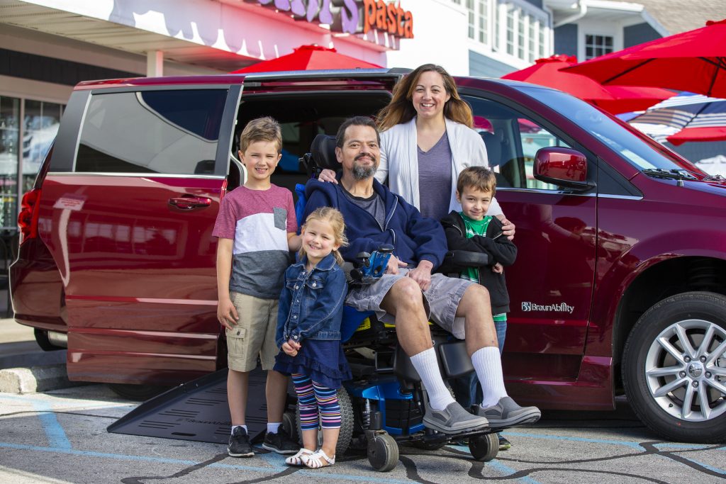 Wheelchair user with family sitting outside wheelchair accessible van posing.